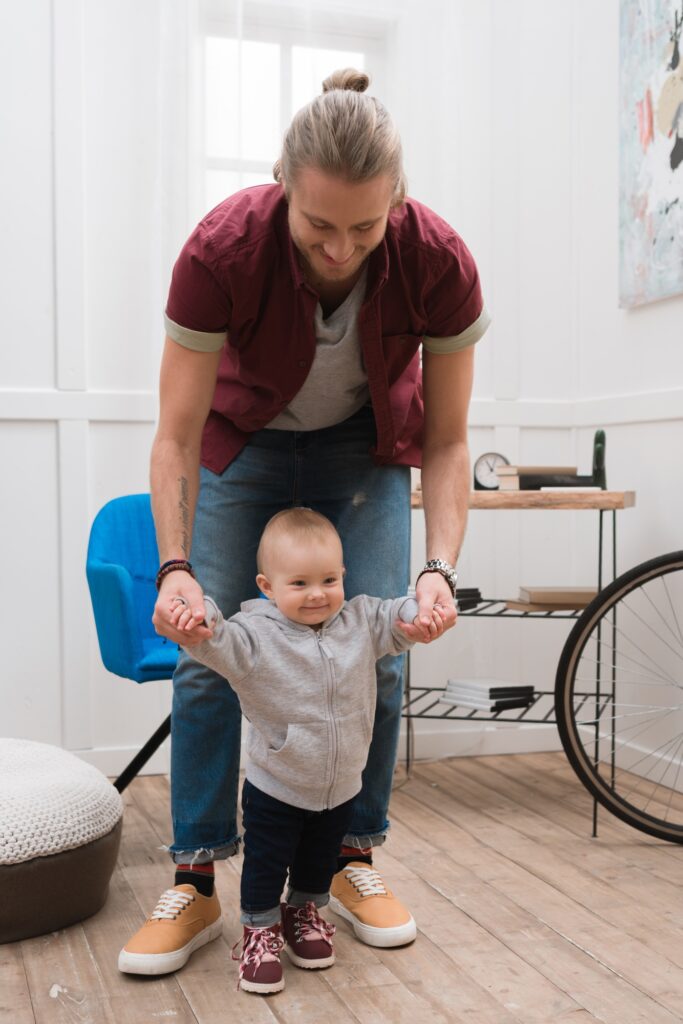 cheerful father teaching baby boy to walk at home