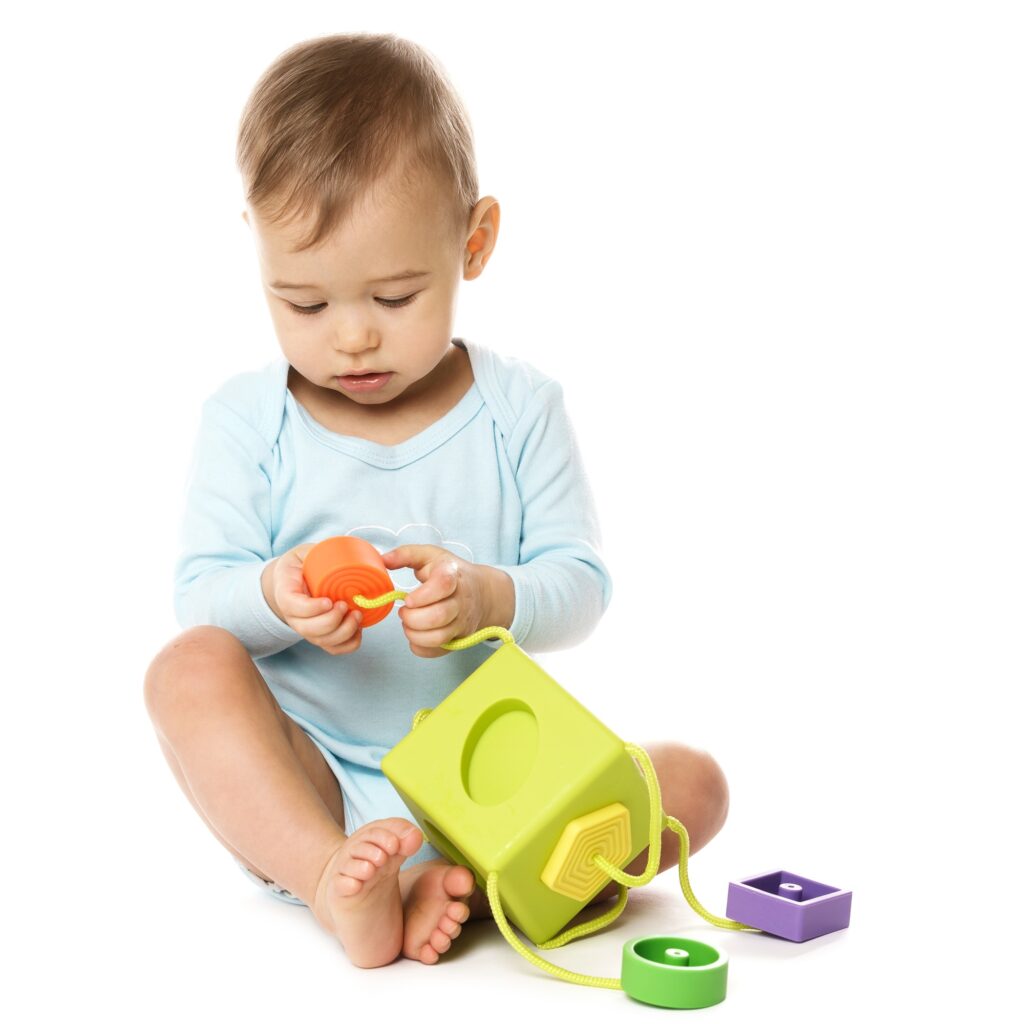 Little boy in romper sitting and playing with plastic toy.