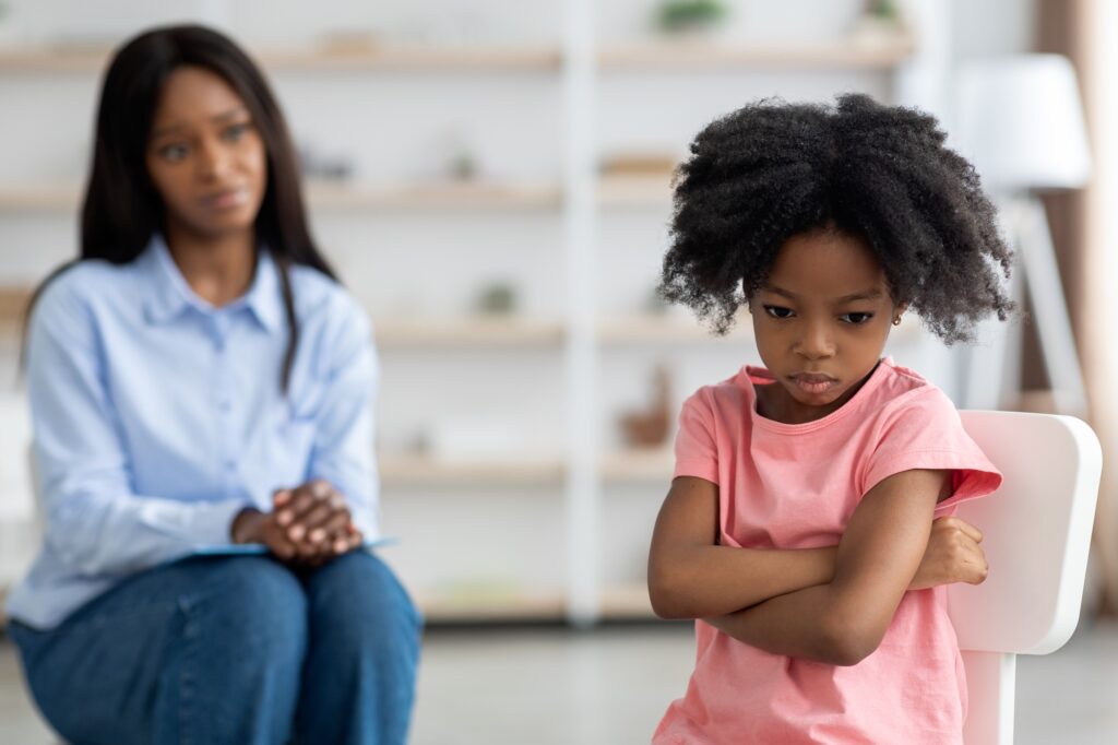 Concerned black woman psychologist looking at angry little girl
