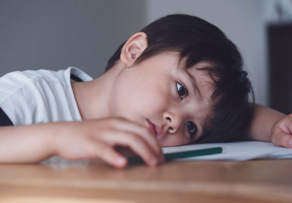 Kid playing colour pencil sitting alone and looking out with sad face,kid bored with school homework