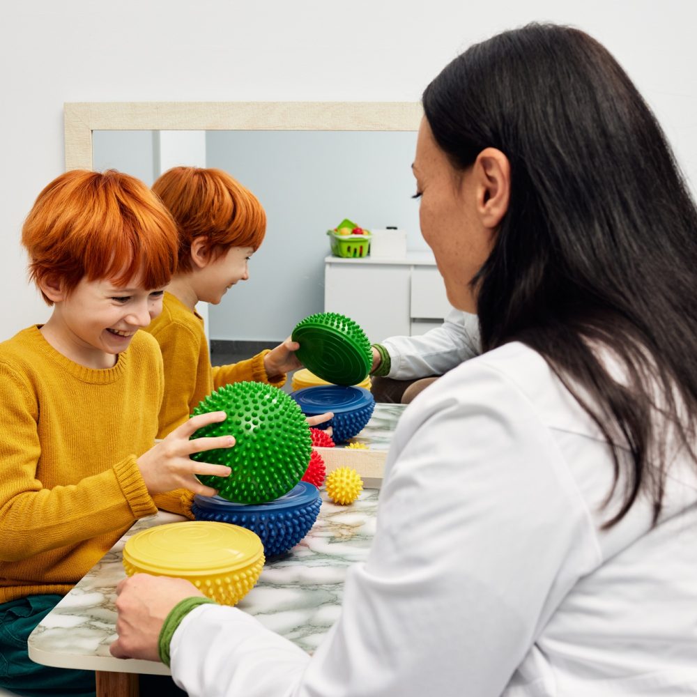 Male child with ASD working with sensory therapist using hedgehog half balls. Sensory integration